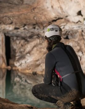 Spéléologie - Femme de dos regardant une étendue d'eau à l'intérieur d'une grotte