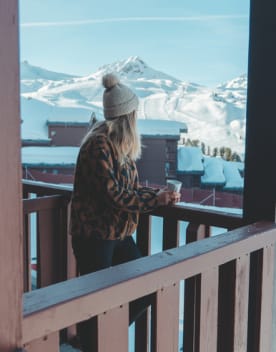 Femme de dos au balcon buvant un café face aux pistes