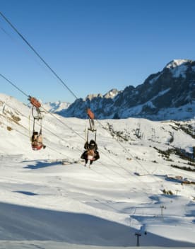 Deux personnes de dos descends en tyrolienne au dessus des pistes enneigées