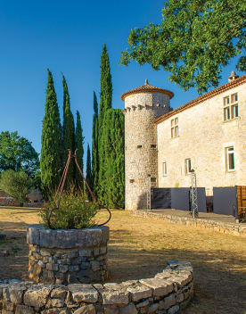 Tour du château de Lou castel sous un ciel bleu en premier plan un ancien puit en pierre fleur - Résidence*** Lou castel - Ardèche