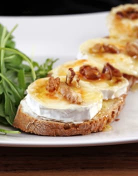 Tartines de fromage de chèvre recouvertes de noix et de miel sur une assiette blanche accompagnées de salade verte