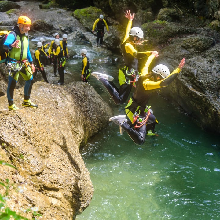 Plusieurs personnes pratiquant le canyoning, sautant dans l'eau entre les roches habillées en combi et casque