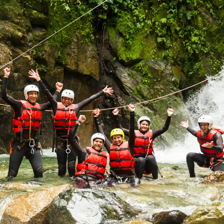 Personnes pratiquant le canyoning posant pour la photo en combi et casque devant une cascade