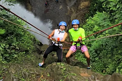 Couple posing with smiles while rappeling down a waterfall