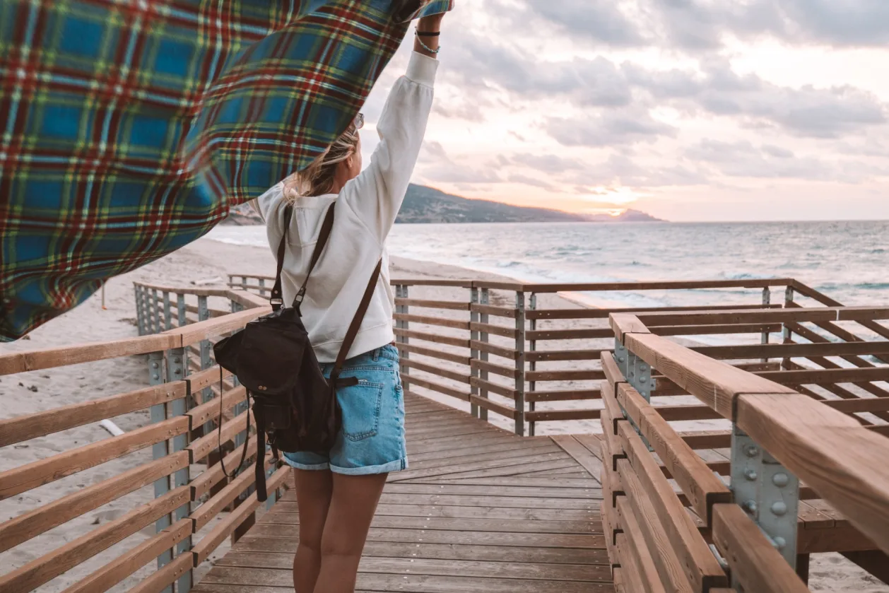 female solo traveler standing on dock with blanket blowing in the wind