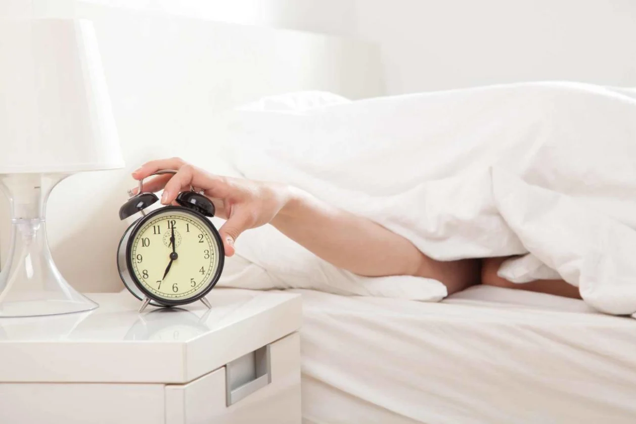 Hand under blanket reaching out for alarm clock trying to beat jet lag