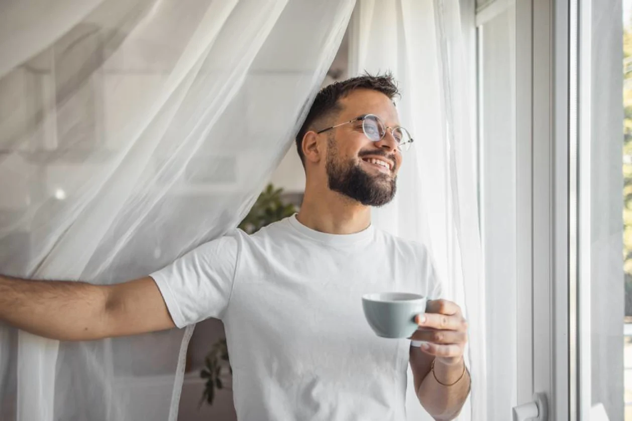 Man enjoying morning coffee standing by window