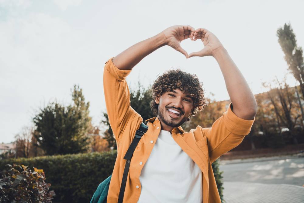 Cheerful man holding hands above head in heart shape