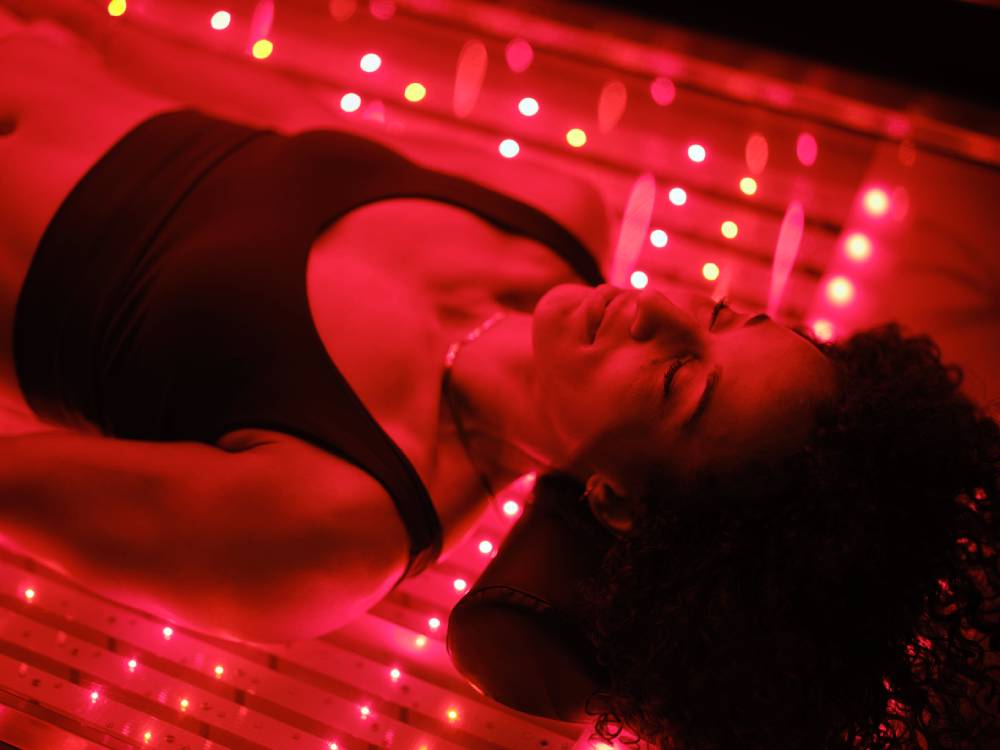 A multiracial woman on an LED light bed, receiving red light therapy as biohacking concept