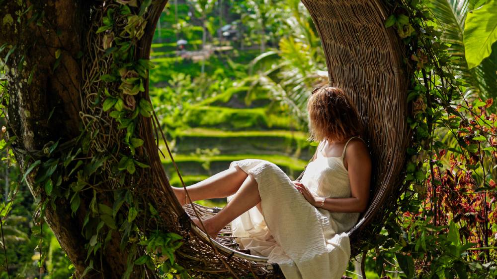 Female tourist in woven nest swing overlooking Tegalalang Rice Terraces Bali