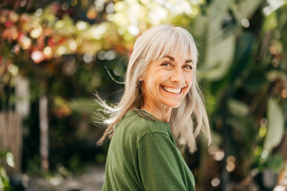 Gray-haired smiling woman amidst trees