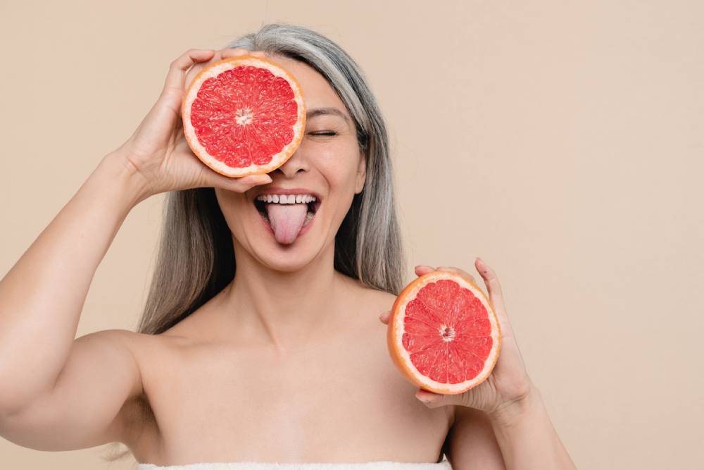 Mature woman with bare shoulders holding grapefruit over eye