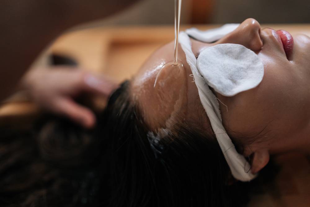 Close up face of woman with cotton pads over eyes while receiving Shirodhara oil treatment