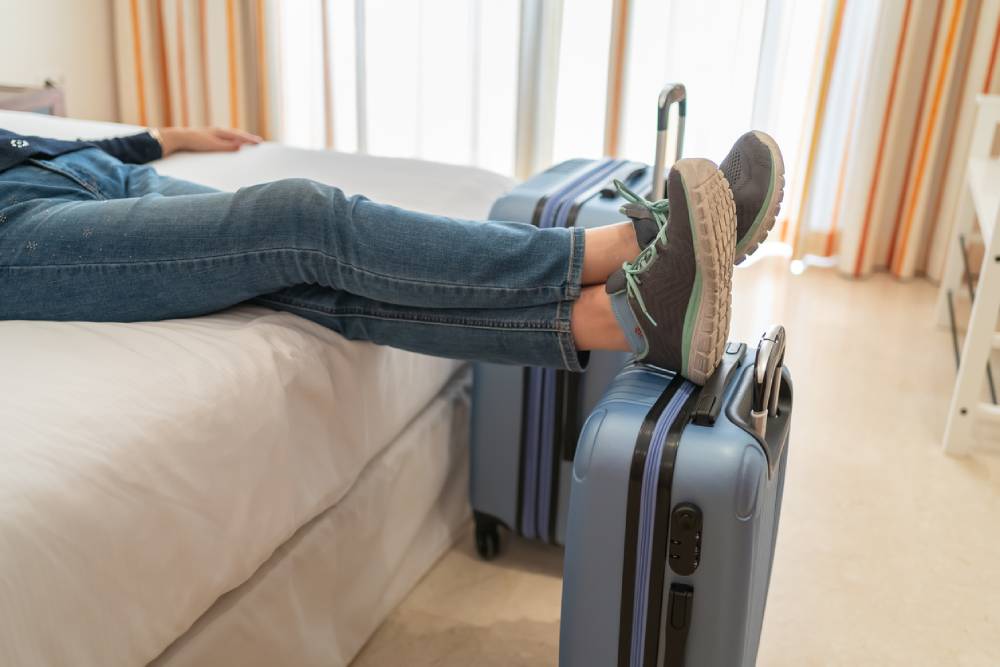 woman traveler lying on hotel bed with feet on suitcase
