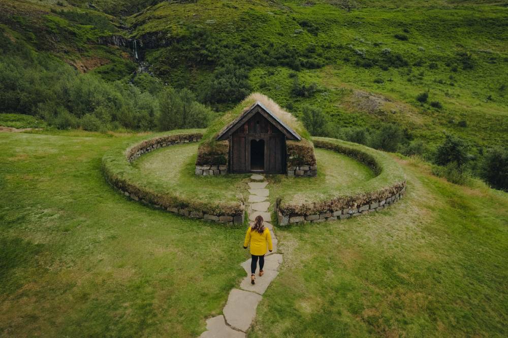 Woman in yellow jacket is walking towards a small hut in Iceland