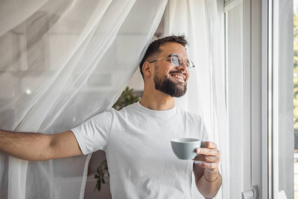 Man enjoying morning coffee standing by window