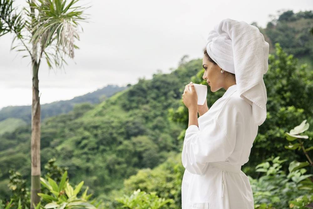 Female guest in bathrobe on balcony sipping tea at The Retreat Costa Rica