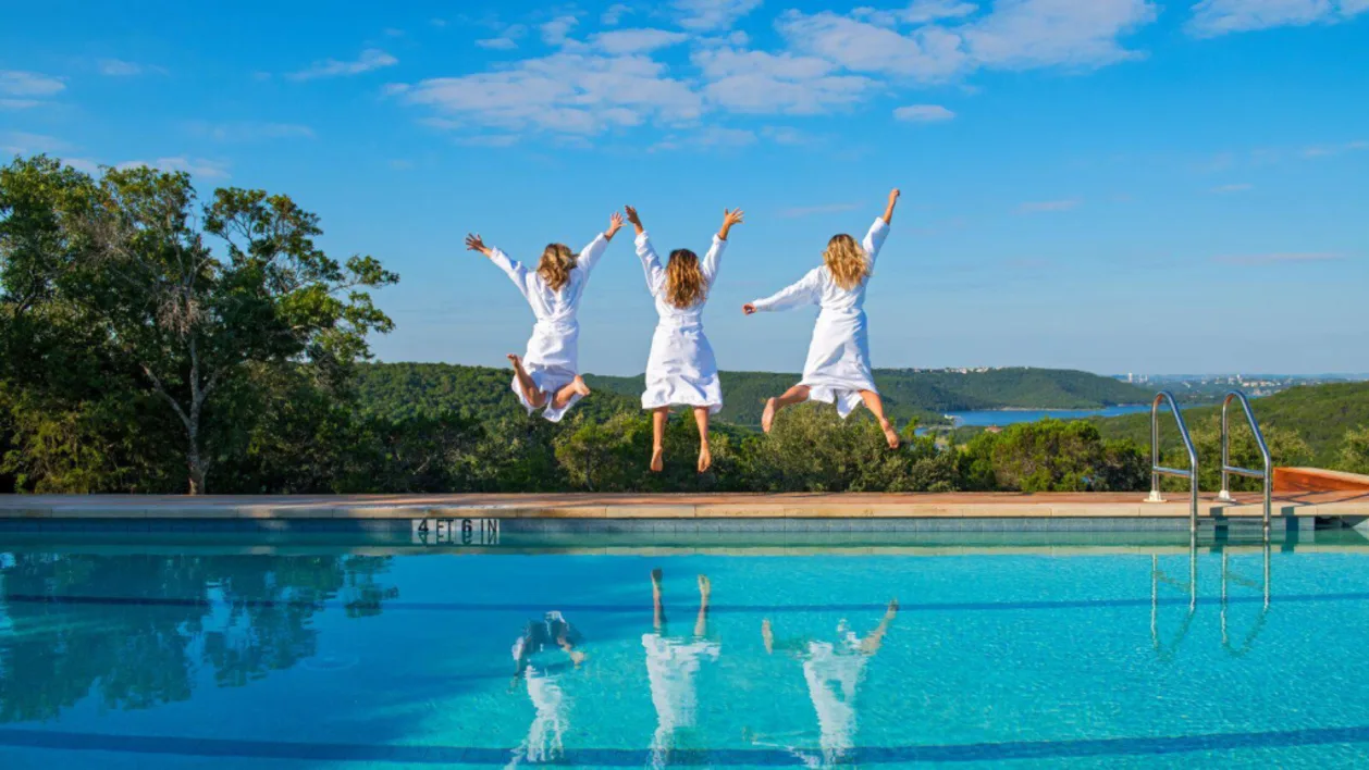 Women in bathrobes jumping near pool at Miraval Austin luxury resort in Texas