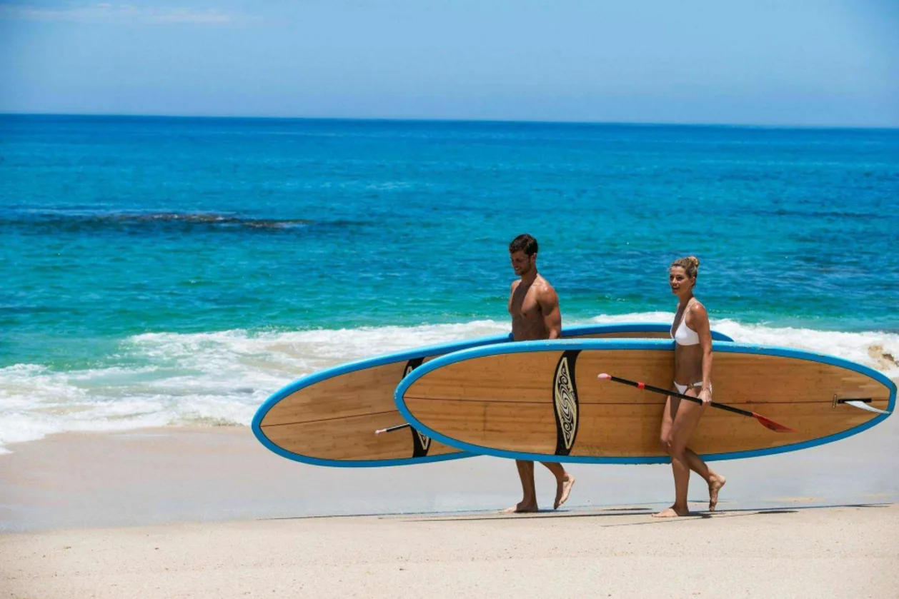 One&Only Palmilla couple with SUP boards walking on beach