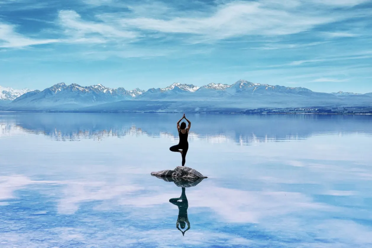 woman practicing intentional yoga tree pose on rock in middle of Lake Tekapo New Zealand