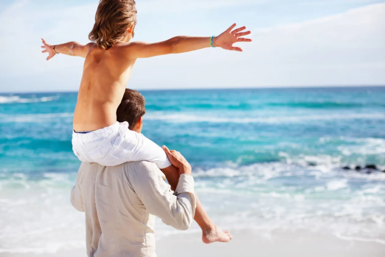 Son balancing on dad's shoulders on beach in family-friendly travel destination Hawaii