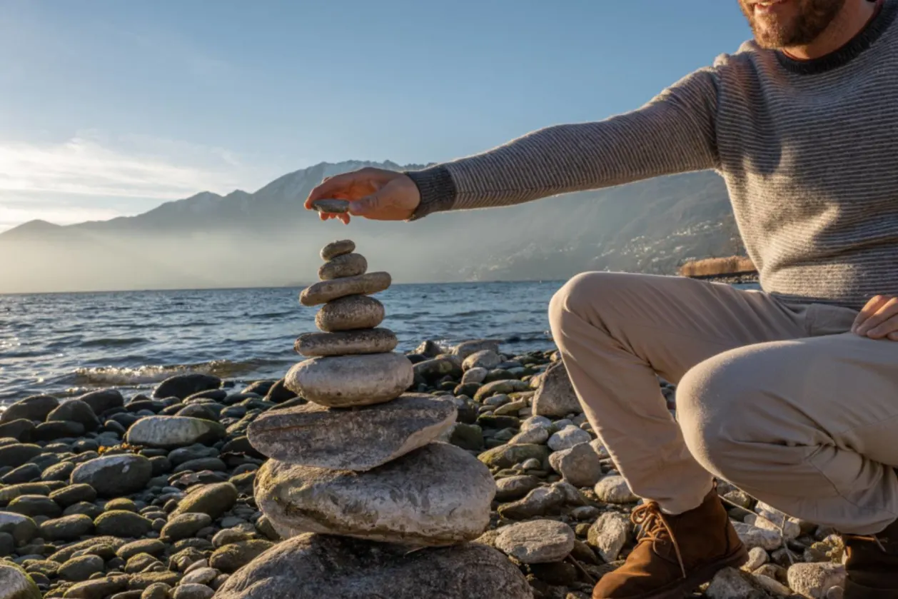 man by lake stacking pebbles