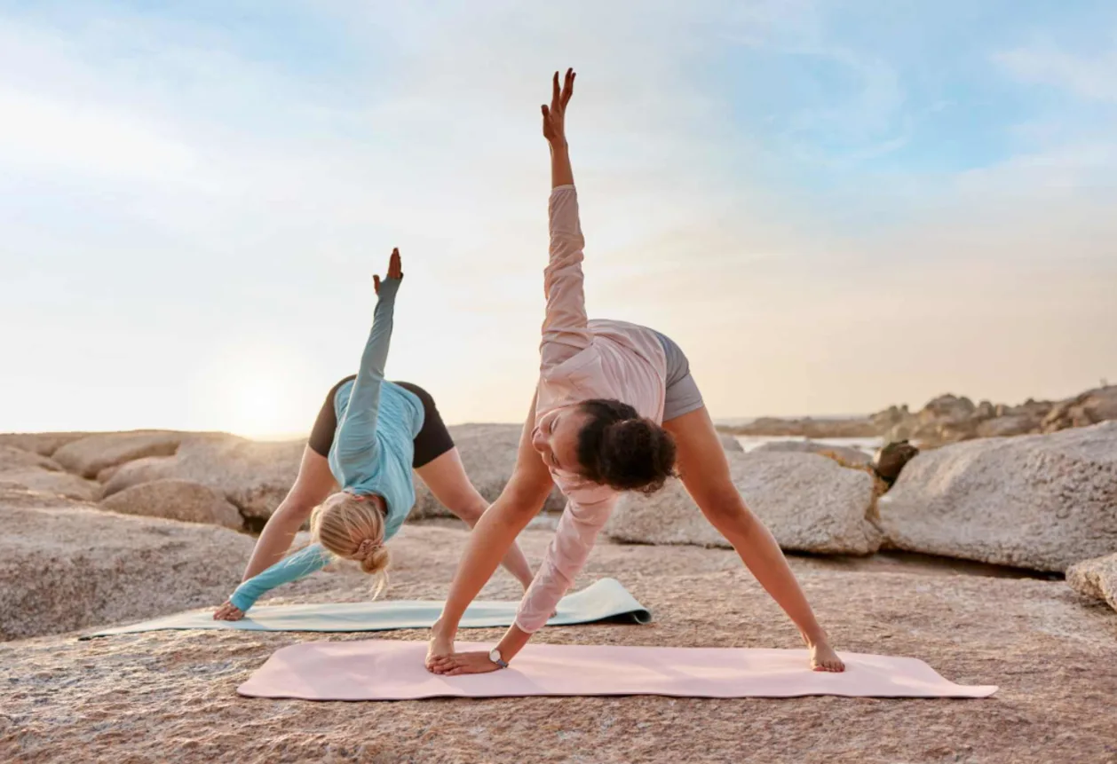 two women practicing yoga on rock at sunset