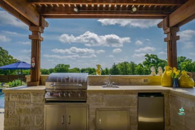 Outdoor kitchen featuring a built-in grill, sink, and stone countertop crafted for a multi-generational family retreat in Springtown, Parker County, TX.