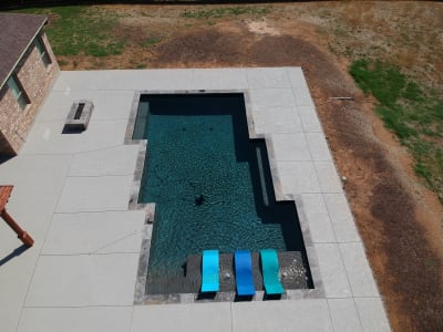 Establishing overview of a custom gunite pool with cedar pergola and dual bubblers crafted on an existing concrete patio in Arlington, Tarrant County, TX.