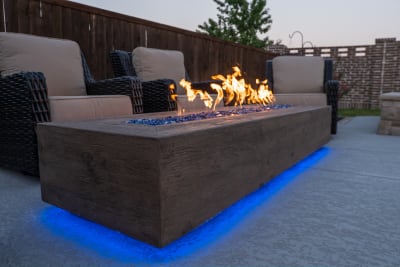 A recessed fire pit with classic fire glass set before a lounge seating area, capturing the refined outdoor living design of a contemporary Roanoke, TX estate.
