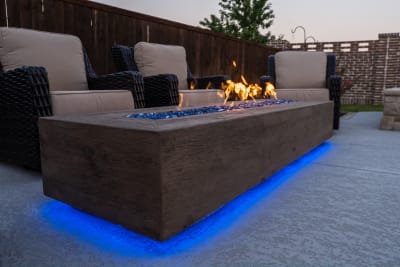 Close-up view of a recessed fire pit glowing with blue-accented lighting on a contemporary patio at a Roanoke, Denton County, TX outdoor living space.