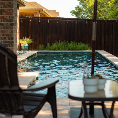 Close-detail view of Light Walnut Travertine coping with eased edge, French pattern concrete paver decking, and stone veneer column at a geometric pool in Arlington, TX.