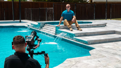 A craftsman pauses on freshly plastered pool steps at the Brumbeloe residence in Keller, TX, with precision decking work visible across the surrounding surface.