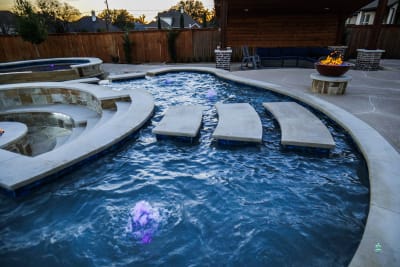 Establishing overview of a resort-style pool with grotto waterfalls, six copper fire bowls, and beach entry in Mansfield, Tarrant County, TX.