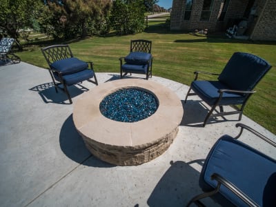 Close-up of a stone-top patio table with integrated fire feature and wood chairs on the Sally Deck at the Cawl Residence in Fort Worth, TX.