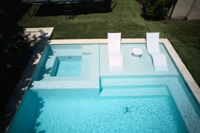 Aerial perspective showcases the seamless integration of tanning ledge and spa within this custom gunite pool design, featuring premium tile accents and stone coping.
