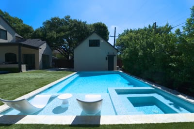 Custom spa seamlessly connects to the main pool via elegant spillover design, featuring premium tile mosaic work throughout the tanning ledge area.