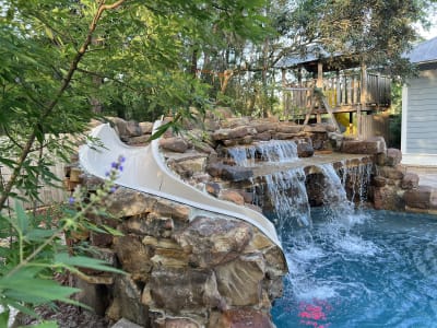 Luxury pool with raised-beam waterfall, sheer descent, spa, and pergola seating area in Santa Rosa Beach, FL.