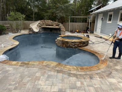 A pool technician maintaining the dark blue plaster interior of the freeform Colon Residence pool, with Oklahoma Stone coping visible along the edge in Santa Rosa Beach, FL.
