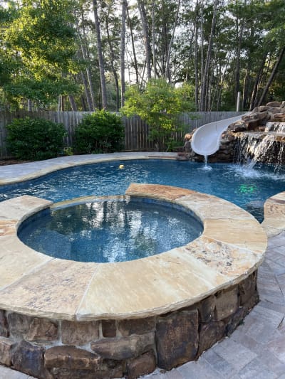 Outdoor pool and spa with waterfall feature, circular stone paver surround, and raised beam lighting at the Colon Residence in Santa Rosa Beach, FL.