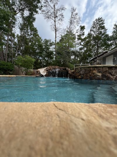 Outdoor swimming pool with brick fountain wall and natural rock backdrop at the Colon Residence in Santa Rosa Beach, FL.