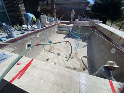 Establishing aerial overview of a contemporary geometric pool with five-layer tiered spillover, Philadelphia Travertine coping, and City Stone Pearl paver deck at a Keller, TX residence.