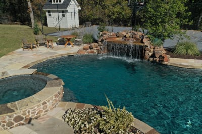 A cascading waterfall feature flowing into a custom pool, framing a natural outdoor living space at a Fort Worth, Tarrant County, TX family retreat.