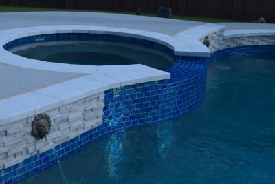 Masterful stone veneer application frames the bronze lion scupper, creating seamless material transitions from travertine ledgestone to custom spa spillover features.