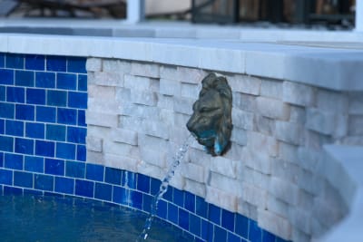 Detailed view of the bronze lion scupper with travertine ledgestone surround, creating a sophisticated water feature that adds movement and sound to this Irving outdoor living space.