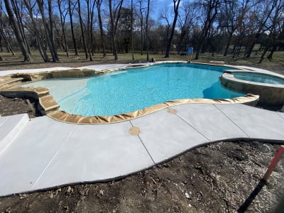 Concrete patio surrounds a freeform pool with custom spa, stone fire pit, and Ecoluxe beach in Anna, TX