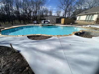Close view of the EcoLuxe beach and composite board walkway meeting the plaster-finish freeform pool edge at a naturalistic retreat in Anna, Collin County, TX.