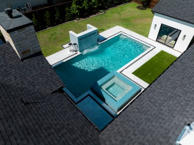 Aerial view of a geometric infinity-edge pool in Colleyville, TX, showcasing Aquabella Madrid Blue raised beam veneer and Aquabella star. Gemini waterline tile against crisp architectural lines.