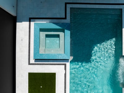 Aerial view of a contemporary geometric infinity-edge pool with Aquabella Madrid Blue raised beam veneer, Gemini waterline tile, and Black Tejas river rock border in Colleyville, TX.