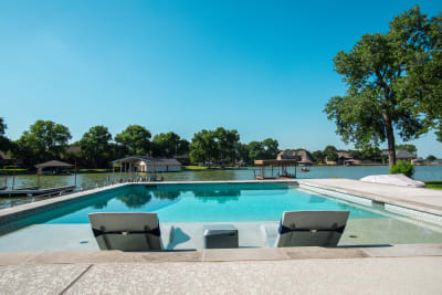Establishing overview of a geometric pool with travertine deck, concrete pavers, aluminum pergola structure, and stainless steel handrails at a Parker County estate in Azle, TX.